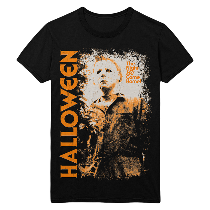 A black short-sleeve graphic t-shirt featuring a distressed orange and white print of Michael Myers from Halloween, with 'HALLOWEEN' written vertically in orange on the left and 'The Night He Came Home' in orange on the right.
